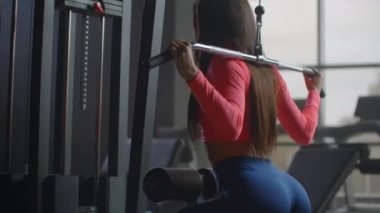 Sabah spor salonunda son derece yoğun bir antrenman. Arka planda geniş pencereleri olan bir odada eğitim gören bir kadın elipsoid ve koşu bandı kullanır.