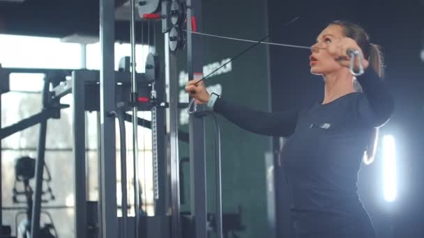 Kvinnan skakar musklerna i bröst och armar i gymmet — Stockvideo