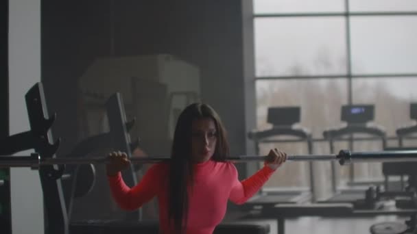 Girl crouches with barbell in gym — Stock Video