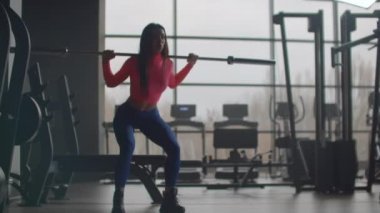 Spor salonunda halterli bir kız çömeliyor.