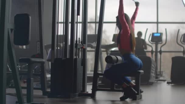 Entrenamiento de fuerza por la mañana en el gimnasio. Entrenamiento en una habitación con grandes ventanas en el fondo una mujer utiliza un elipsoide y una cinta de correr — Vídeo de stock