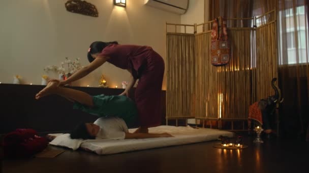 Asian Woman utför traditionell thailändsk massage till vacker europeisk kvinna. Rehabilitering och behandling efter skador med hjälp av massage. Slappna av och vila från massage av ben, armar och rygg. — Stockvideo