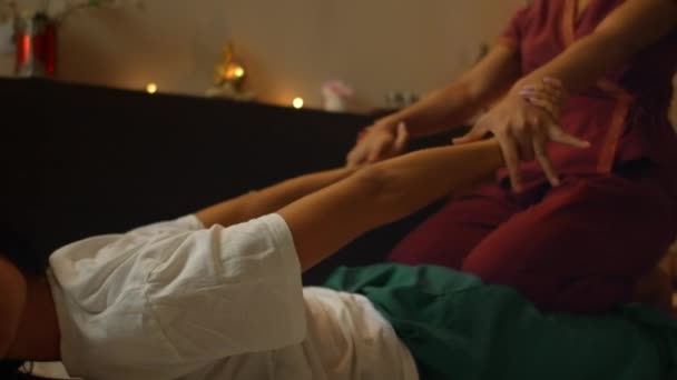 Asiatico donna esegue tradizionale tailandese massaggio a bella europeo donna. Riabilitazione e trattamento dopo lesioni con l'aiuto del massaggio. Relax e riposo dal massaggio di gambe, braccia e schiena . — Video Stock