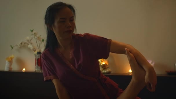 Asiatische Frau führt traditionelle thailändische Massage für schöne europäische Frau durch. Rehabilitation und Behandlung nach Verletzungen mit Hilfe von Massage. Entspannung und Erholung von der Massage der Beine, Arme und Rücken. — Stockvideo