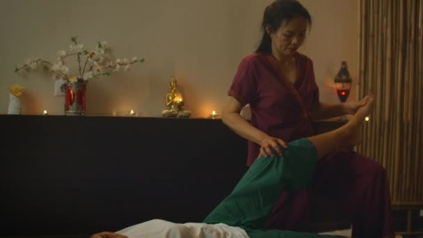Asiatico donna esegue tradizionale tailandese massaggio a bella europeo donna. Riabilitazione e trattamento dopo lesioni con l'aiuto del massaggio. Relax e riposo dal massaggio di gambe, braccia e schiena . — Video Stock
