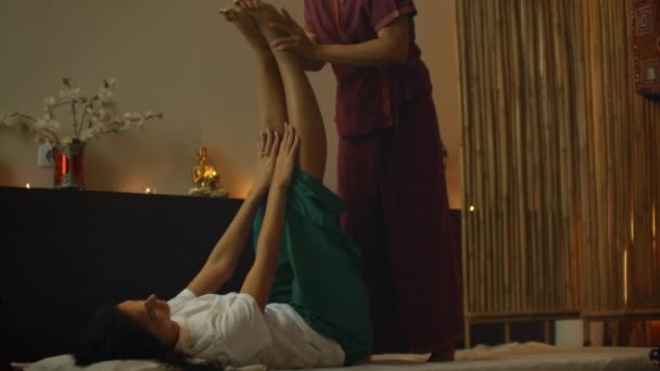 Asian Woman utför traditionell thailändsk massage till vacker europeisk kvinna. Rehabilitering och behandling efter skador med hjälp av massage. Slappna av och vila från massage av ben, armar och rygg. — Stockvideo