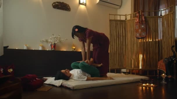 Mujer asiática realiza masaje tailandés tradicional a la hermosa mujer europea. Rehabilitación y tratamiento después de lesiones con la ayuda de masaje. Relájese y descanse del masaje de piernas, brazos y espalda . — Vídeo de stock