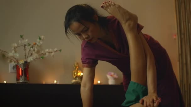 Junge Frau genießt traditionelle thailändische Massage, bei der ihr Rücken gedehnt wird. gleitender Ausschnitt eines professionellen thailändischen Masseurs, der sich nach hinten seiner Frau ausstreckt — Stockvideo