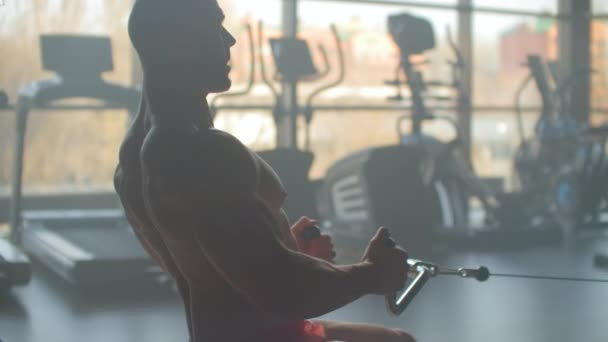 En trött sportiga mannen sitter på den inomhus Roddaren på gym. personer och fitness koncept — Stockvideo