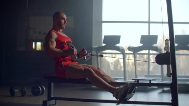 En trött sportiga mannen sitter på den inomhus Roddaren på gym. personer och fitness koncept — Stockvideo