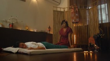 Geleneksel Thai masajından hoşlanan, sırtı gerilmiş genç bir kadın. Profesyonel bir Tayland masörünün dişisinin arkasını gererken kaydı.