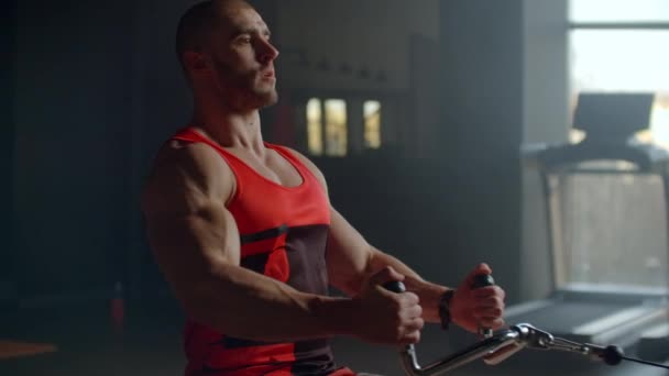 Joven haciendo ejercicios en la espalda con una máquina de ejercicios de poder en un club de gimnasia. Al hombre atlético haciendo los entrenamientos a la espalda con la máquina de ejercicios de fuerza en el gimnasio en el fondo de las ventanas grandes — Vídeos de Stock