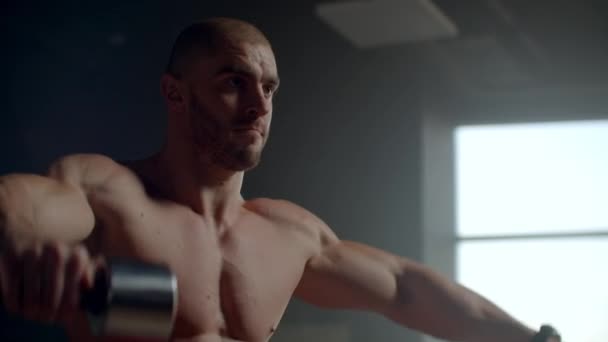 Brutal hombre levanta pesas en el gimnasio entrenando su espalda y hombros. Hermoso club de fitness con grandes ventanas — Vídeos de Stock