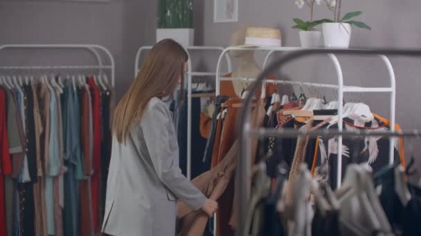 Compras, moda, estilo e conceito de pessoas - mulher feliz escolhendo roupas e olhando para espelhar no shopping ou loja de roupas . — Vídeo de Stock