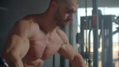 Genç adam spor salonundaki simülatörde el kesimi yapıyor. Göğüs kasları için egzersiz. Çapraz.