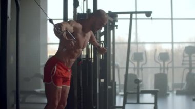 Vücut geliştirici göğüs kaslarını çalıştırmak için kablo çapraz makine kullanıyor ve kameraya bakıyor, ön görüş. Karanlıkta spor salonunda beyaz duman. Spor motivasyonu. Mükemmel vücutlu, çıplak gövdeli bir model.