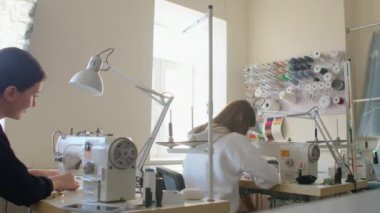 Elbise dikme atölyesinde dikiş makinelerinde çalışan iki kadın terzi. Tasarımcı elbiselerinin yaratılışı. Küçük bir iş. İki çalışan arkadan dikiş makineleri üzerinde çalışıyor..