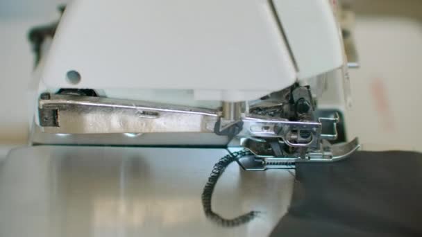 Close-up, de bijnaaimachine passeert de randen van de zwarte stof in slow motion. Serger proces in de naaiatelier. — Stockvideo