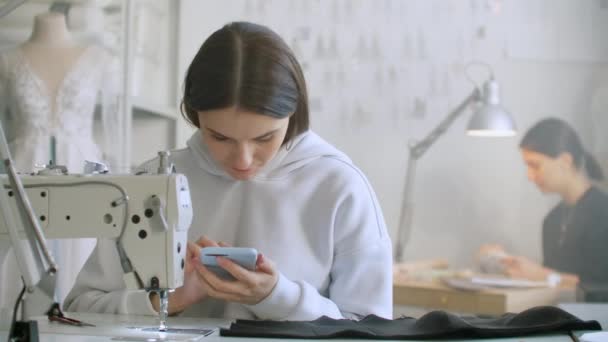 Женщина-швея смотрит на экран смартфона на рабочем месте. Запись текстовых сообщений клиентам — стоковое видео