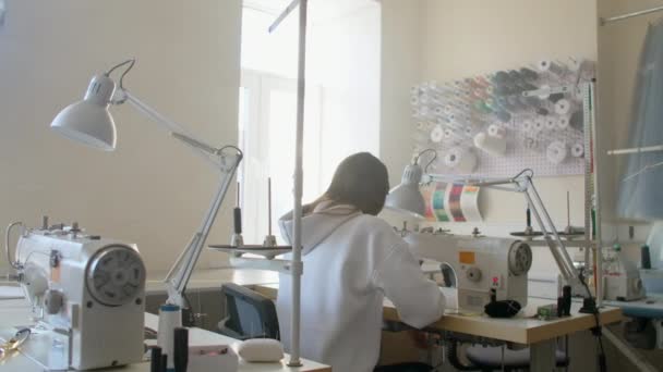 Donna sarta che lavora in un laboratorio di cucito dietro una macchina da cucire vista posteriore. Indietro ragazze cucitrici nella produzione di macchine per cucire — Video Stock