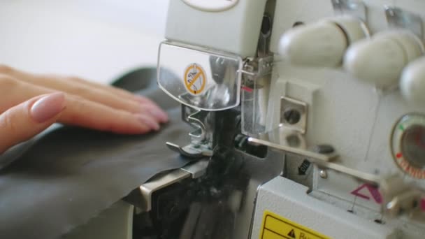 Close-up, de bijnaaimachine passeert de randen van de zwarte stof in slow motion. Serger proces in de naaiatelier. — Stockvideo