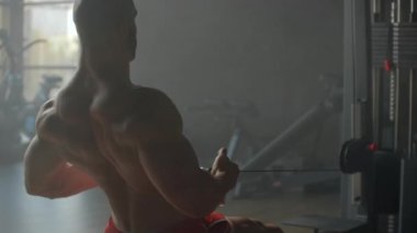 Bir adam simülatörde oturup sırt kasları için spor salonunun geniş pencerelerine karşı egzersiz yaparken karnına ağırlığını koyar. Güçlü erkek sporcu kürek çekiyor. 