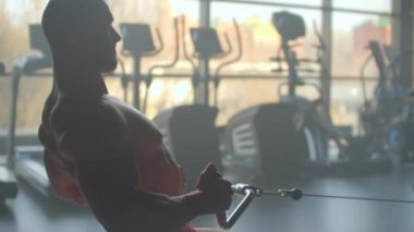 Simülatörde ağırlık egzersizi yapan bir sporcu büyük bir pencere spor salonunun arka planında oturan çıtayı çeker. Kasıtlı olarak arkadan atlet görüşü.