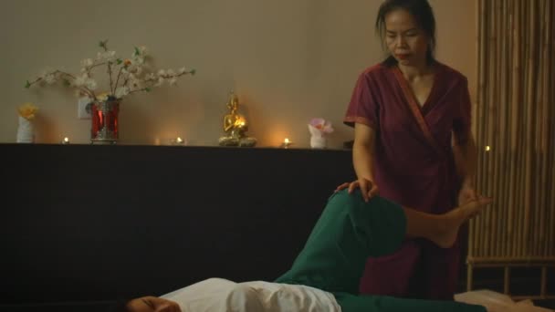 Азиат выполняет массаж в национальной одежде Таиланда. Азиатский Спа салон в Европе. Молодая белая женщина расслабляется во время массажа — стоковое видео
