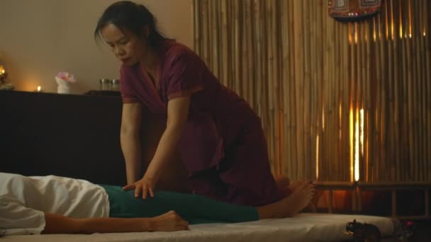 Азиатка делает традиционный тайский массаж на спине лежащей красивой европейской девушки. Хиропрактик производит лечение альтернативными методами — стоковое видео