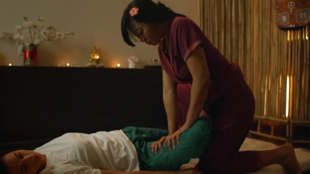 Salón de masajes tailandés. Mujer asiática en ropa tradicional haciendo masaje relajante terapéutico, mujer caucásica. Masaje tradicional profesional. Medicina alternativa — Vídeos de Stock