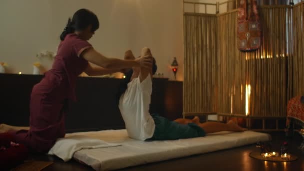 Medicina alternativa chinesa, uma mulher asiática realiza massagem terapêutica nas costas e pernas de uma mulher caucasiana deitada em um sofá. Aromaterapia e terapia manual por mestres chineses — Vídeo de Stock