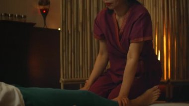 Asyalı, Tayland 'ın ulusal kıyafetleriyle masaj yapıyor. Avrupa 'daki Asya Spa Salonu. Genç beyaz kadın masaj yaparken rahatlıyor.