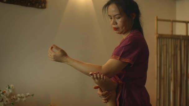 一位亚洲妇女在躺在沙发上的一位白人妇女的背上和腿上进行治疗性按摩，这是一种替代疗法。 中国大师的芳香疗法和手工疗法 — 图库视频影像