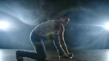 Modern bale, sahnede oturan bir adam sahne ışıklarının altındaki dumanın altında kameraya dönerek takla atar. Modern koreografi tiyatro sahnesinde..