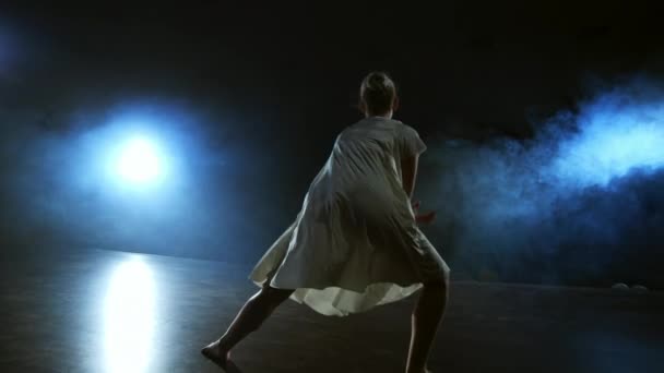Modern balenin dramatik bir sahnesi, beyaz elbiseli yalnız bir balerin modern koreografiyi kullanarak dans adımları atıyor. — Stok video