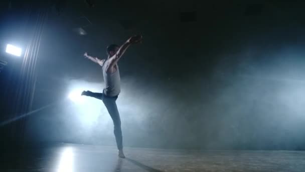 Un ballet moderno, un hombre realiza saltos y giros a la luz de focos y humo sobre un fondo oscuro. Coreografía acrobática, ensayo del guion del ballet moderno — Vídeo de stock