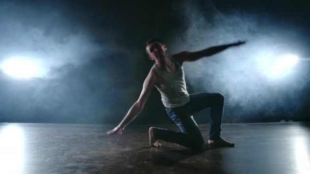 Сучасний балет, чоловік з сидячого положення на сцені стрибає назад з обертанням на темній сцені в диму в центрі уваги — стокове відео
