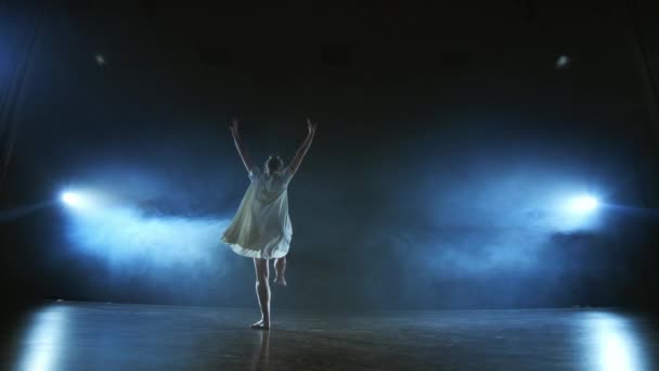 Dramatic spins and flips of a modern ballet dancer from a musical. A single woman emotionally dances on stage against a dark background with smoke in the spotlight in slow motion — Stock Video