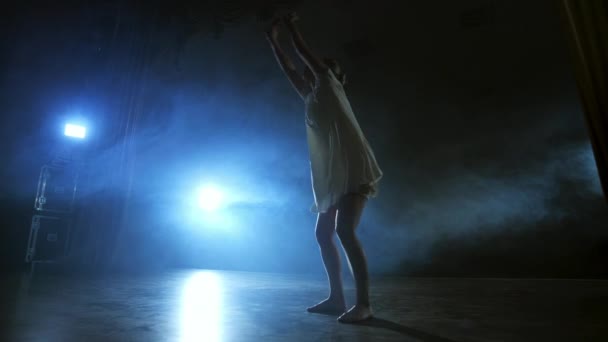 Драматична сцена сучасного балету, самотня балерина в білій сукні виконує танцювальні кроки з використанням сучасної хореографії — стокове відео
