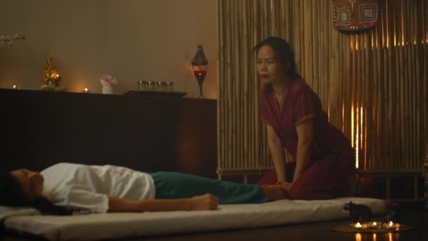 En asiatisk kvinna utför en traditionell thailändsk massage på baksidan av en ljugande vacker europeisk flicka. Kiropraktor producerar behandling med alternativa metoder — Stockvideo
