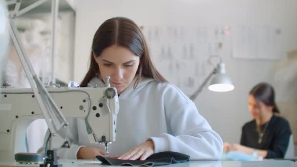 Mujeres jóvenes manos costurera sentado y cose en la máquina de coser en el estudio de diseño creativo. Dos jóvenes empresaria modista haciendo nuevo . — Vídeo de stock