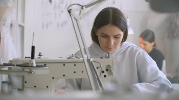 Alfaiataria de roupa. Estresses de costura no trabalho na oficina que cose a roupa na máquina que cose. Os fabricantes de vestidos cosem a roupa no atelier. Duas mulheres costureiras. Dressmaking no negócio de costura — Vídeo de Stock