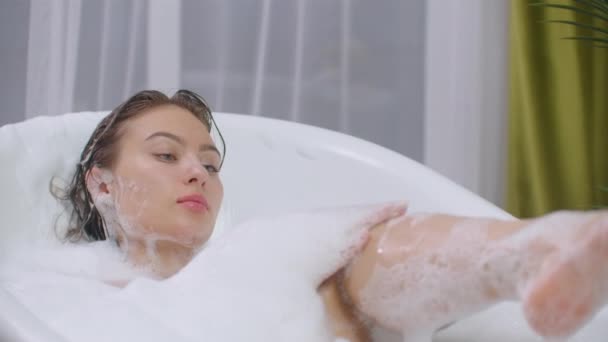 A beautiful brunette woman lies in a bubble bath and rests from a working day — Stock Video