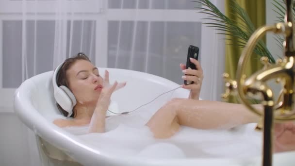 Mulher bonita ouvindo música na banheira desfrutando de relaxante banho de espuma estilo de vida real natural cuidados com o corpo . — Vídeo de Stock
