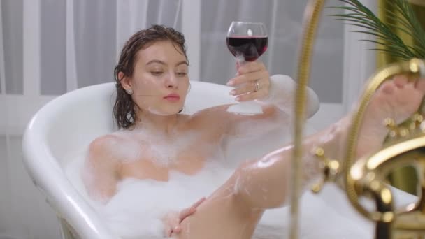 하얀 욕조에 누워서 붉은 포도주 한 잔으로 긴장을 풀라. 따뜻하게 쉬고 있는 욕조에서 휴식을 취하고 있는 젊은 여자 — 비디오