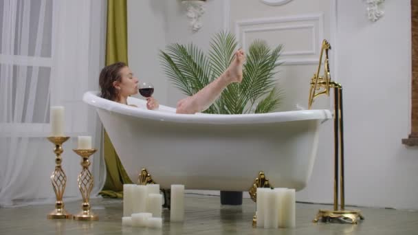 Rilassatevi in un bagno bianco con un bicchiere di vino rosso. Giovane donna rilassante in bagno caldo rilassante — Video Stock