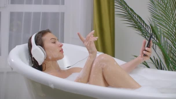 Όμορφη γυναίκα ακούγοντας μουσική στην μπανιέρα απολαμβάνοντας χαλαρωτικό τρόπο ζωής αφρόλουτρο πραγματική φυσική φροντίδα του σώματος. — Αρχείο Βίντεο
