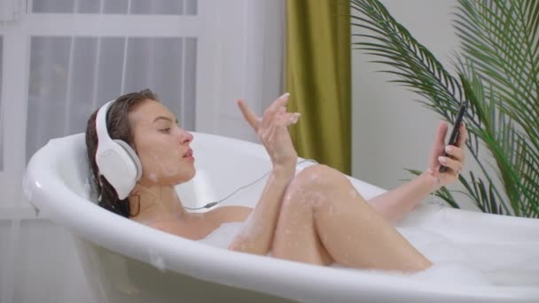 Mulher bonita ouvindo música na banheira desfrutando de relaxante banho de espuma estilo de vida real natural cuidados com o corpo . — Vídeo de Stock