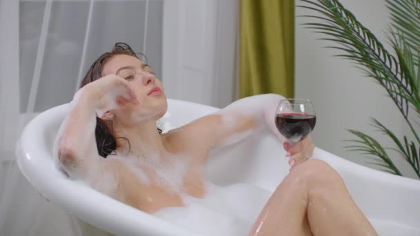 Beba vino tinto tumbado en un baño caliente de burbujas y escuche música para relajarse. Acuéstese y reponga fuerzas después de una semana ocupada de trabajo — Vídeos de Stock