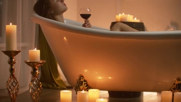 Schönes Mädchen in einer Badewanne mit Kerzen in Gläsern auf dem Boden und flauschigen Federn auf einem weißen Tisch. — Stockvideo
